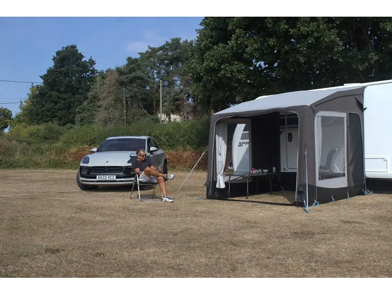 Telta Pure 260 Vorzelt mit geöffneter Front am Wohnwagen, daneben sitzt eine Person vor einem geparkten Auto