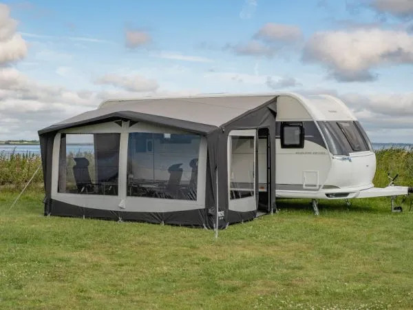 Seitlich aufgebautes Telta Estate 390 Vorzelt an einem Wohnwagen auf einer Wiese mit Blick auf große Panoramafenster