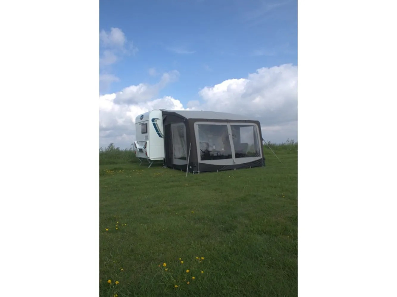 Telta Pure 390 Vorzelt am Wohnmobil aus der Distanz auf einer weitläufigen Wiese unter blauem Himmel