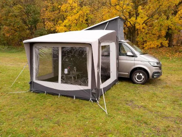 Schrägansicht des Telta Core 260 Busvorzelts am Kastenwagen mit großen Fensterflächen auf einer herbstlichen Wiese