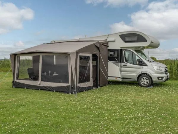 Großzügiges Telta Core 390 Busvorzelt seitlich an einem Wohnmobil aufgebaut auf einer grünen Wiese mit viel Platz im Innenraum