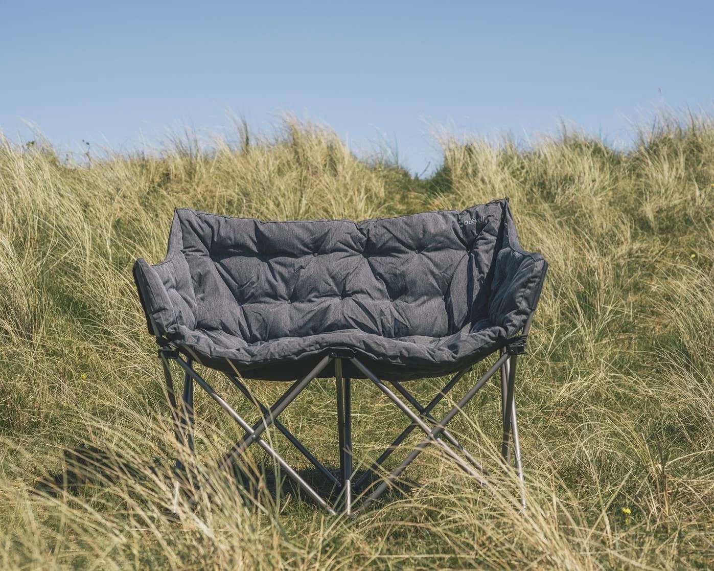 Outwell Sardis Lake Sofa als gepolstertes Campingsofa zwischen Dünengras im Outdoor-Einsatz.