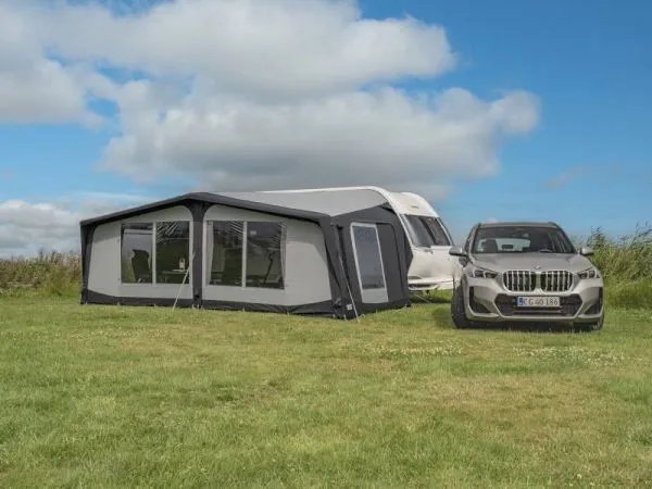 Aufgebautes Telta Apex Luftvorzelt Größe 20 auf dem Campingplatz neben Wohnwagen und abgestelltem Fahrzeug