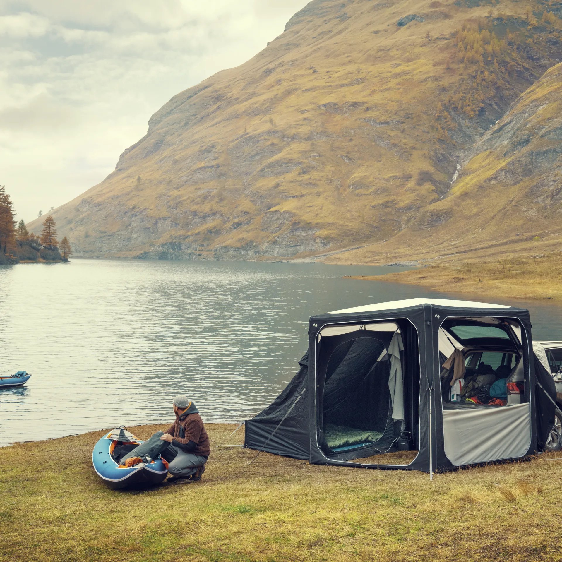 Outdoor Szene am See mit Dometic Hub Pavillon am Fahrzeug waehrend eine Person ein Kajak vorbereitet vor Berglandschaft