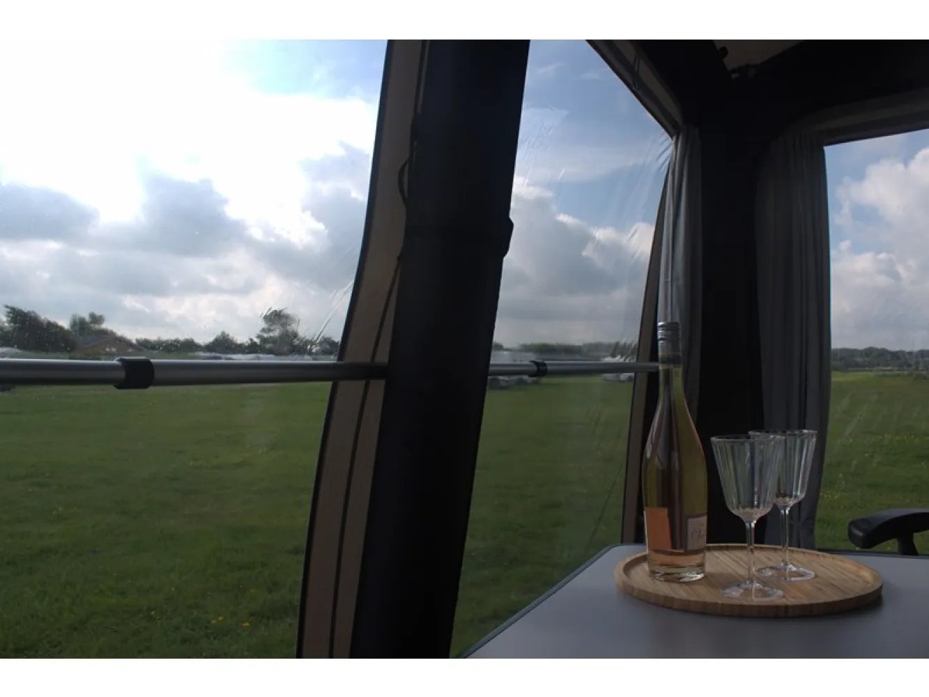 Innenansicht des Telta Pure 390 Vorzelts mit Blick durch das Fenster auf eine grüne Wiese und gedecktem Tisch im Vordergrund