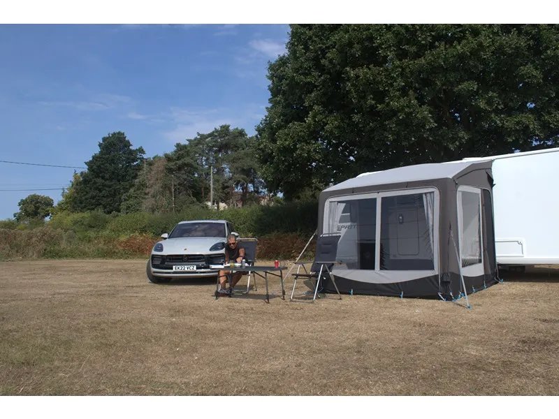 Camping-Szene mit Telta Pure 260 Vorzelt am Wohnwagen sowie Tisch, Stühlen und geparktem Auto daneben
