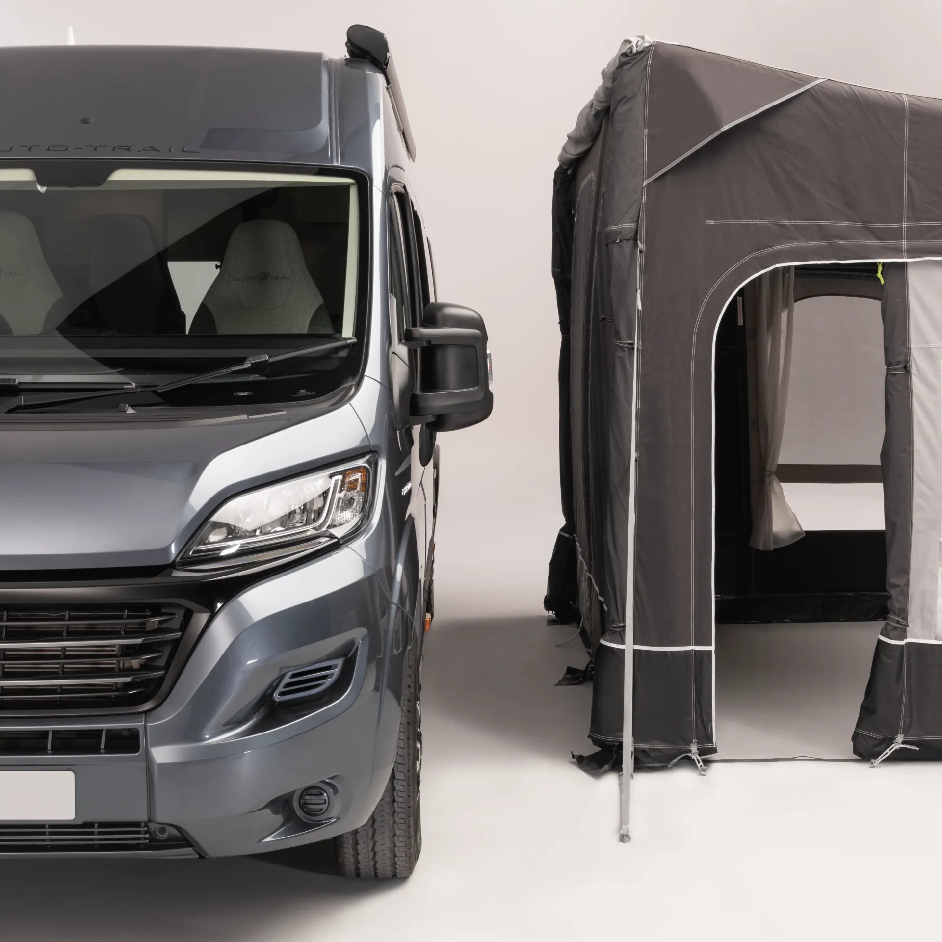 Frontansicht eines Wohnmobils neben einem freistehenden Dometic Rally AIR All Season 330 Drive Away Vorzelt mit geöffnetem Eingang freigestellt auf weißem Hintergrund