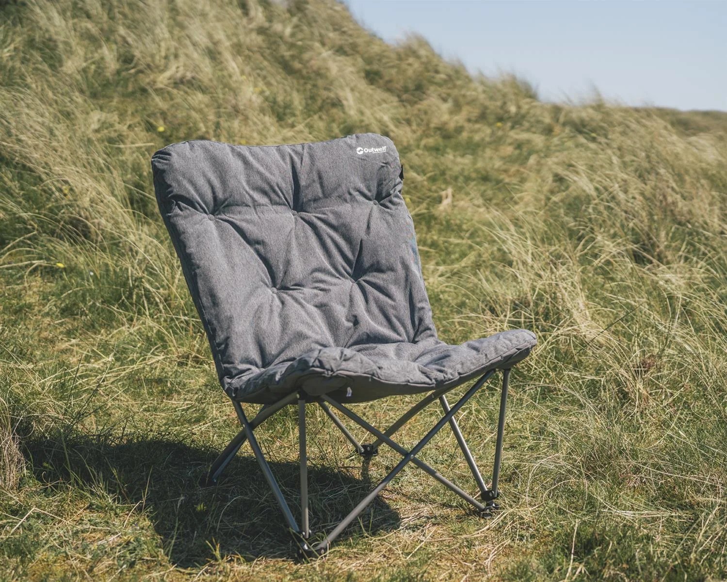 Zwischen Dünen und hohem Gras steht der Outwell Fremont Lake Stuhl als bequemer Campingstuhl für entspannte Pausen bereit.
