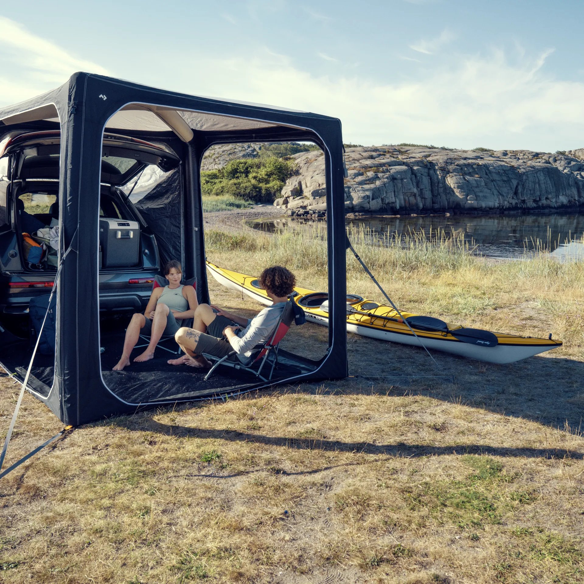 Entspannte Campingszene mit Dometic Hub Pavillon am Wasser neben Fahrzeug und Kajak in natuerlicher Umgebung