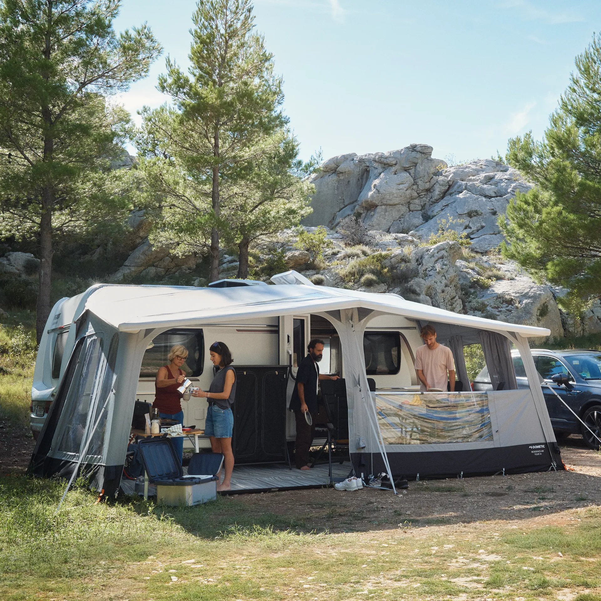 Dometic Residence AIR Tour 18 Vorzelt im Einsatz beim Camping mit mehreren Personen vor einem Wohnwagen in naturnaher Umgebung