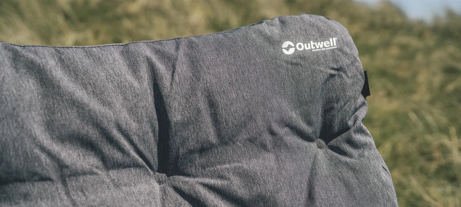 Im Gras der Düne setzt das Kopfpolster des Outwell Fremont Lake Stuhl mit Logo und weichem Bezug einen klaren Fokus.