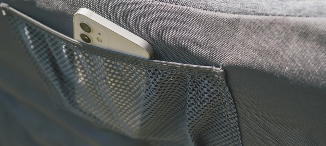 Ein Smartphone steckt im Netzfach des Outwell Fremont Lake Stuhl und zeigt die praktische Aufbewahrung am Sitzmöbel.