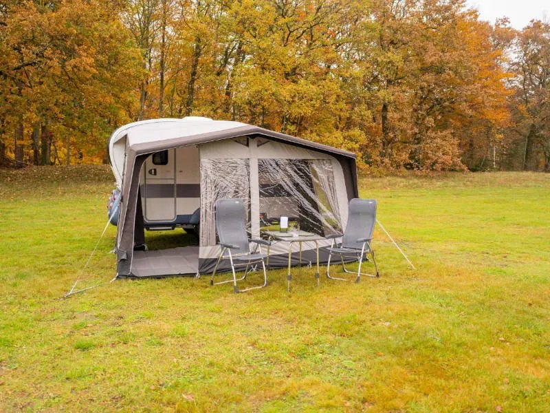 Schrägansicht des Telta Action 361/391 Wohnwagen Vorzelts mit Sitzgruppe vor dem Eingang auf herbstlicher Wiese