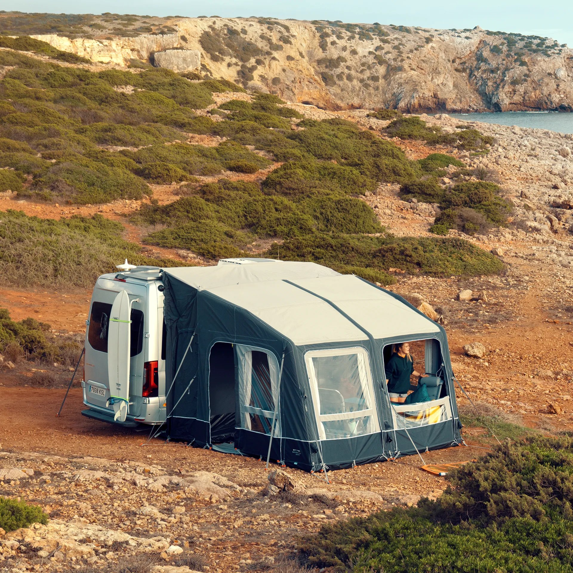 Camping-Szene an der Küste mit aufgebautem Dometic Rally AIR All Season 330 Drive Away Vorzelt an einem Wohnmobil, umgeben von Felsen und Vegetation