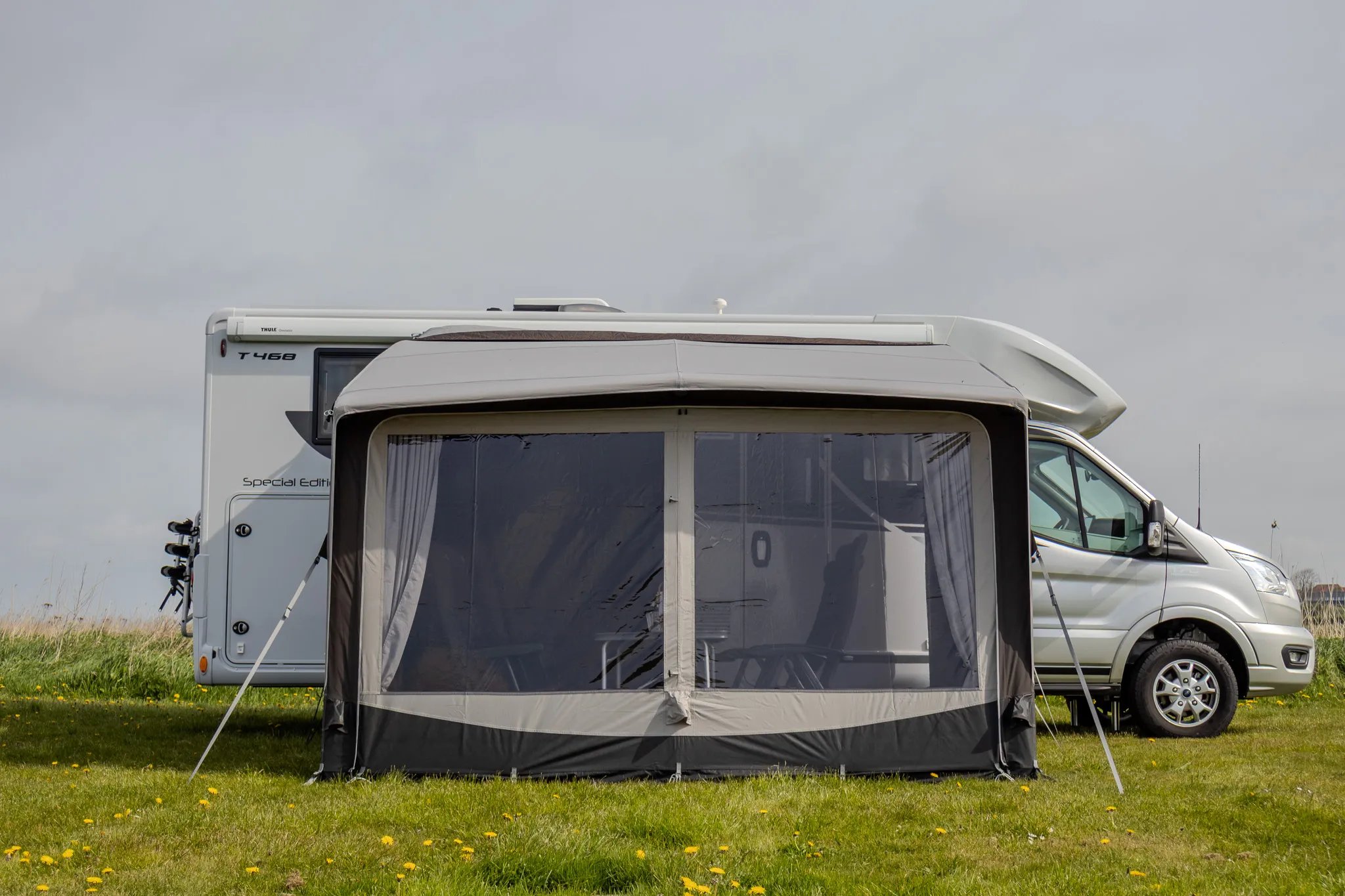 Frontansicht des Telta Core 330 Busvorzelts mit großer Panoramafront und Blick auf den angeschlossenen Kastenwagen auf der Wiese