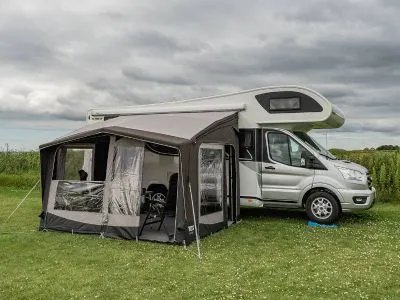 Telta Life 330 Busvorzelt mit teilweise geöffneten Seitenwänden an einem Wohnmobil auf einer Wiese unter bewölktem Himmel