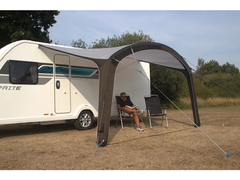 Telta Sky 400 Vorzelt als offenes Sonnendach am Wohnwagen mit Sitzplatz und entspannter Person darunter auf der Wiese