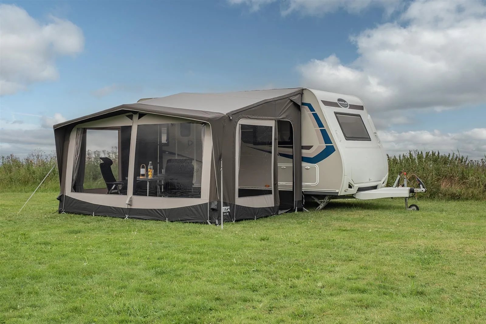 Seitlich aufgebautes Telta Life 390 Vorzelt an einem Wohnwagen auf einer Wiese mit großen Panoramafenstern und Eingangsbereich