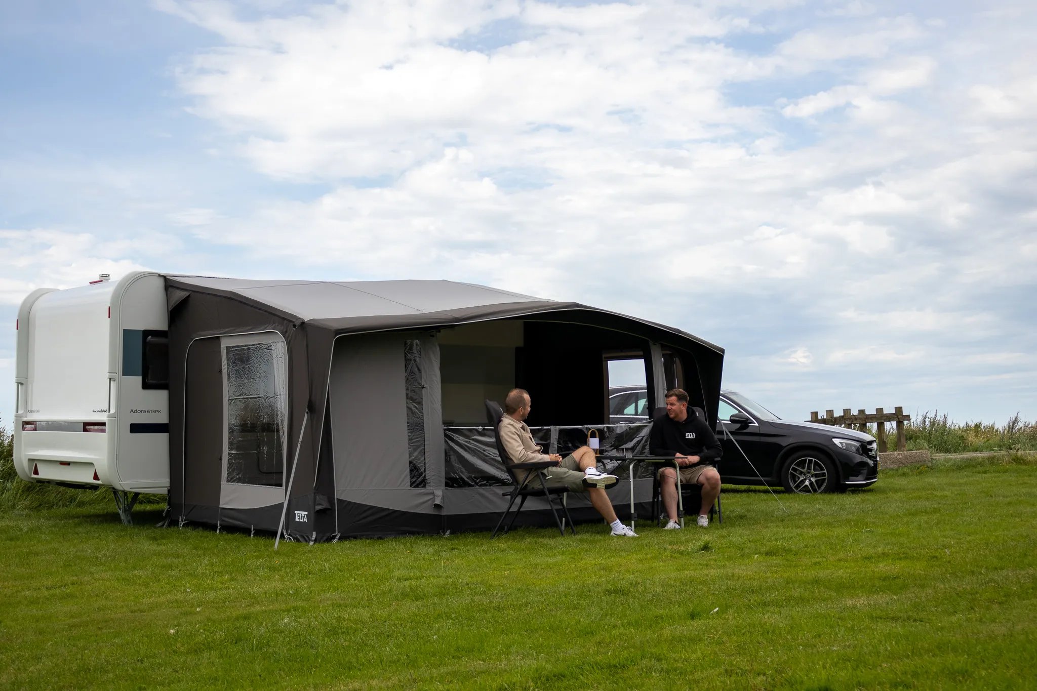 Geöffnete Front beim Telta Scenic 490 Vorzelt mit Sitzgruppe davor und zwei Personen auf der Wiese