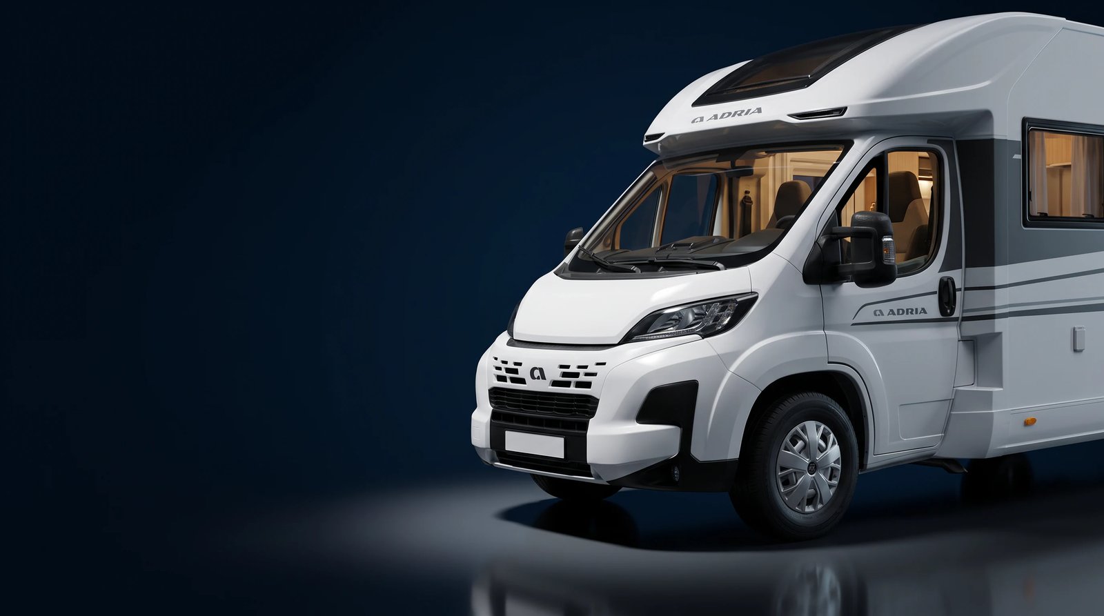 Weißes teilintegriertes Adria Reisemobil im Studiolicht, Frontpartie schräg von vorn, das Fahrerhaus warm beleuchtet