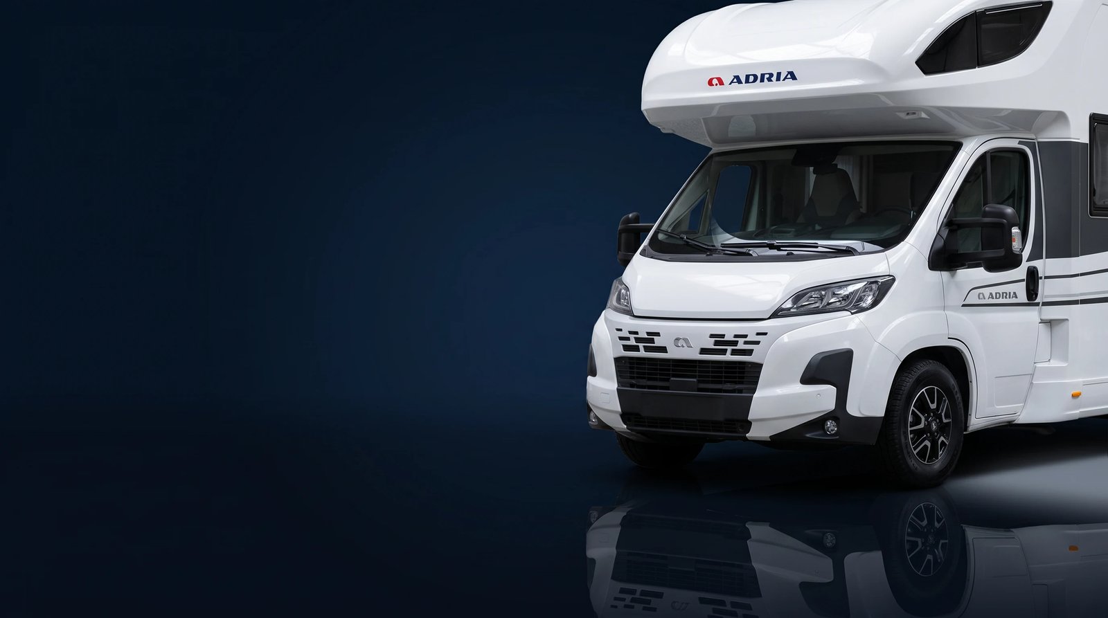 Weißes Adria Alkoven-Reisemobil im Studiolicht, Frontpartie schräg von vorn