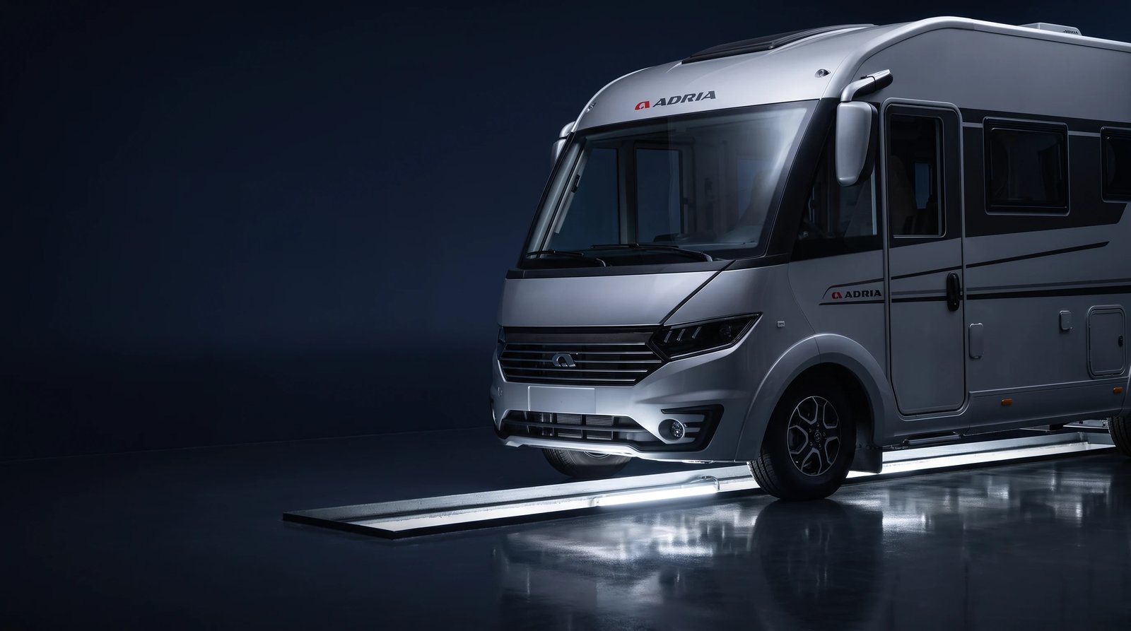 Silbergraues integriertes Adria Reisemobil in der Werkstatthalle, Frontpartie schräg von vorn
