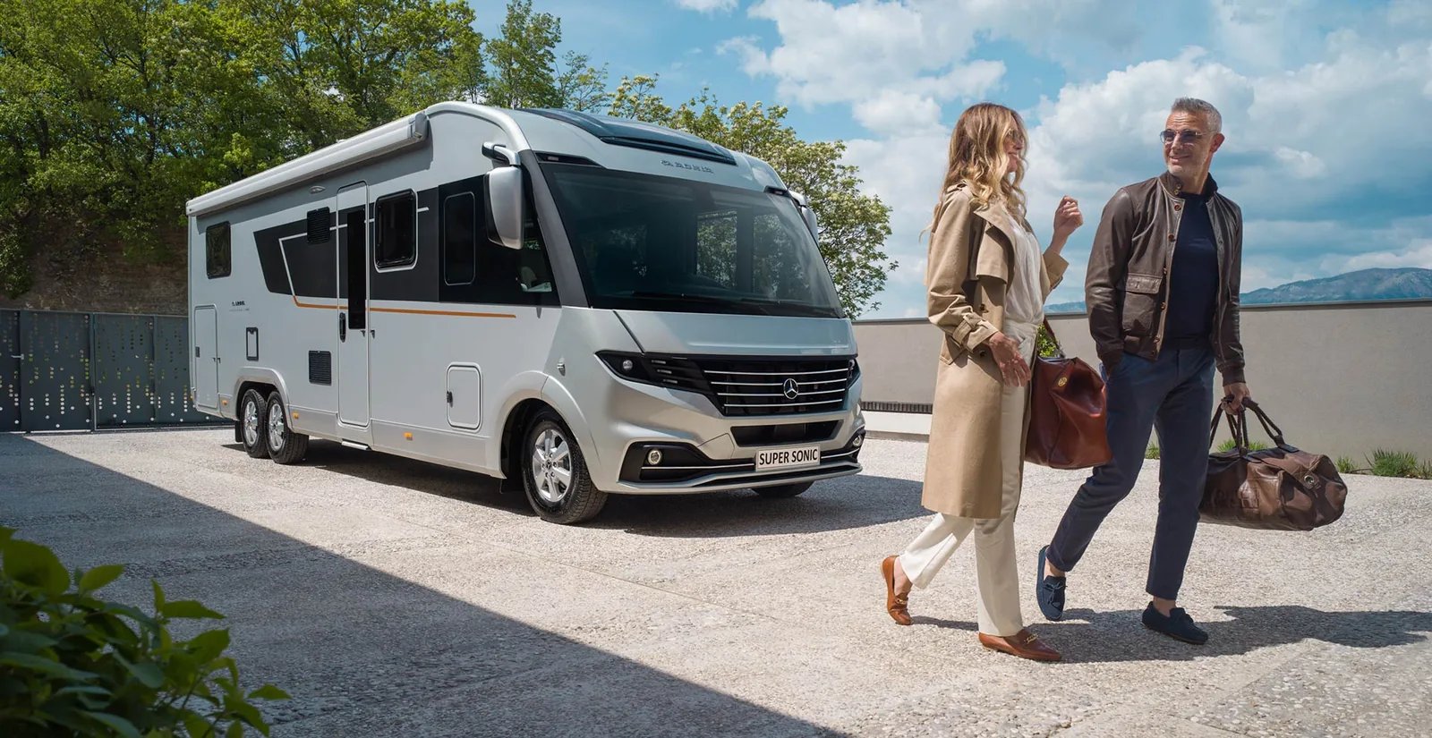 Adria Supersonic 2026 - elegant gekleidetes Paar beim Spaziergang neben dem Wohnmobil in Seitenansicht