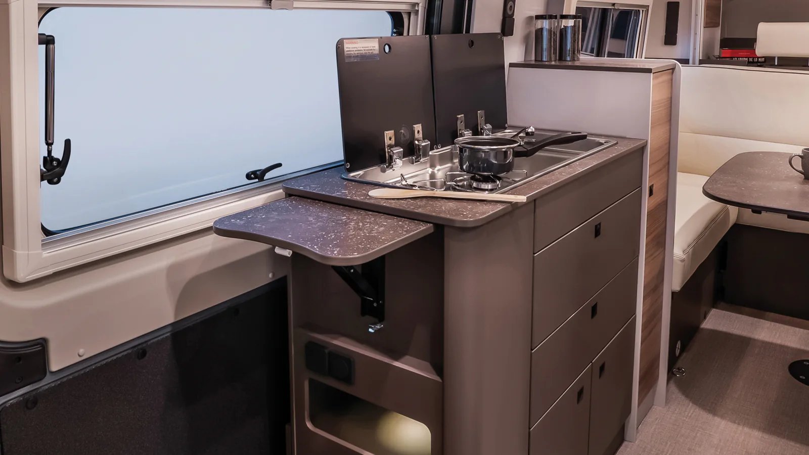 Küchenzeile im Bürstner B66 Camper Van mit geöffneten Glasdeckeln, Zweiflamm-Gaskocher, Spüle und ausgeklappter Arbeitsplattenverlängerung