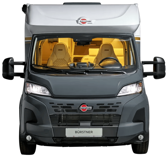 Bürstner B66 Wohnmobil in der Frontansicht mit eingeschalteten Scheinwerfern, breiten Außenspiegeln und beleuchtetem Fahrerhaus