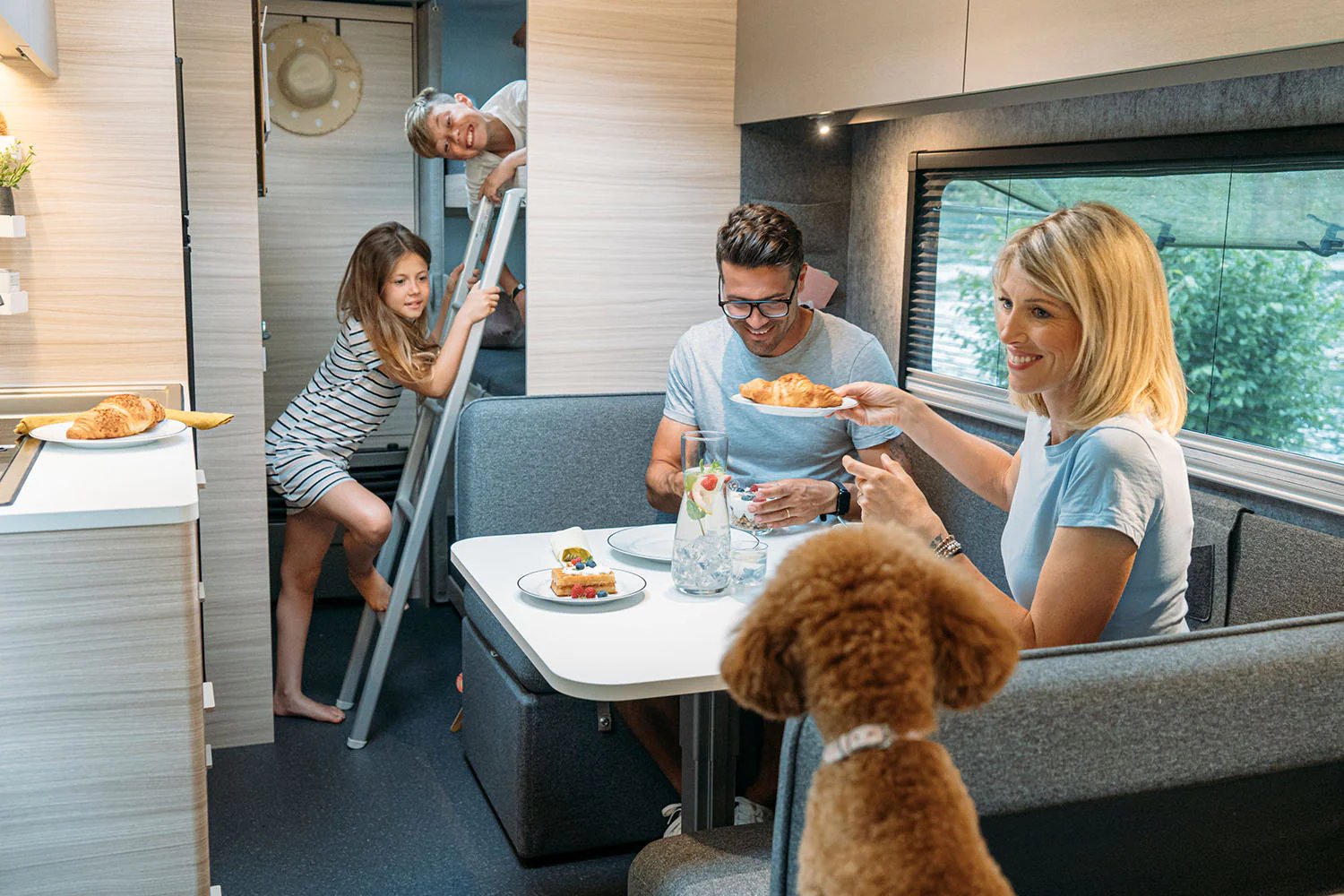 Familie beim Frühstück in der Dinette des Adria Altea, Kinder klettern zum Etagenbett, Hund sitzt mit am Tisch