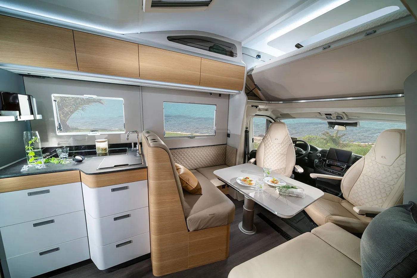 Adria Coral XL 2026 - hochgeschwenktes Alkovenbett über der Fahrerkabine mit Blick auf den Wohnraum darunter