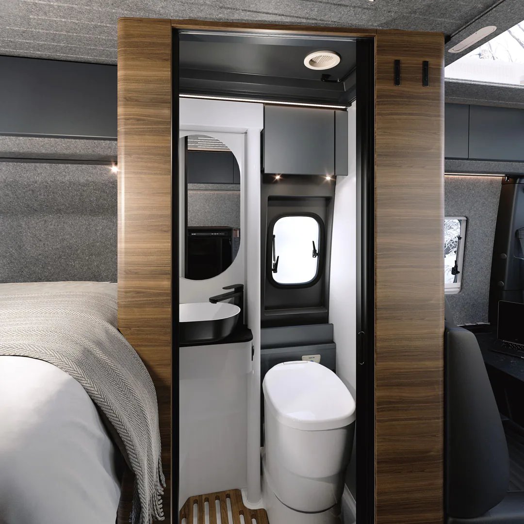 Adria Supertwin 2026 - Badezimmer mit geöffneter Tür, Toilette und Holzdekor neben dem Bett