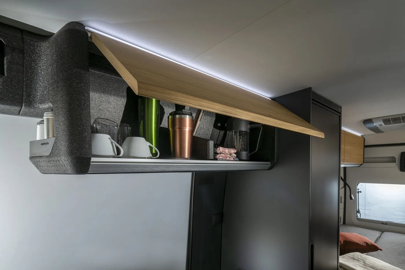 Adria Twin Select 2027 - geöffneter Oberschrank in heller Holzoptik über der Küchenzeile