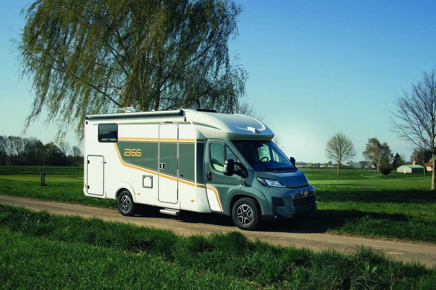 Bürstner B66 Wohnmobil in Dreiviertelansicht von vorn rechts auf einem Feldweg zwischen Wiesen, Markisenkassette und Zierstreifen sichtbar