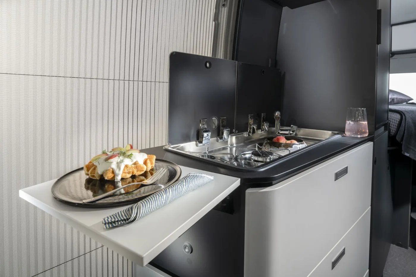 Adria Twin Supreme 2027 - Küche mit ausziehbarer Arbeitsflächenerweiterung, anthrazitfarbenen Fronten und mattweißen Oberschränken