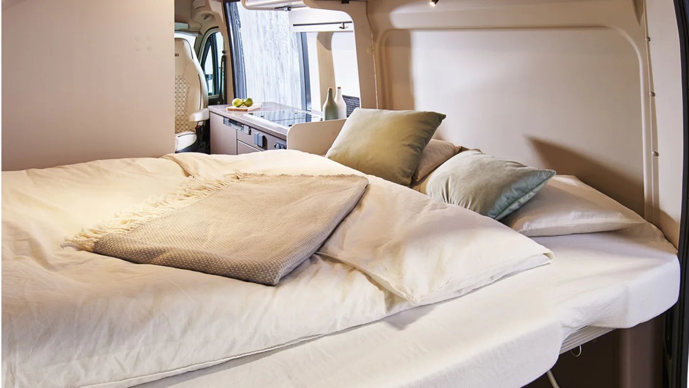 Blick vom Heckbett quer durch den Wohnraum des Bürstner B66 Camper Van auf Küchenblock und gedrehten Fahrerhaussitz