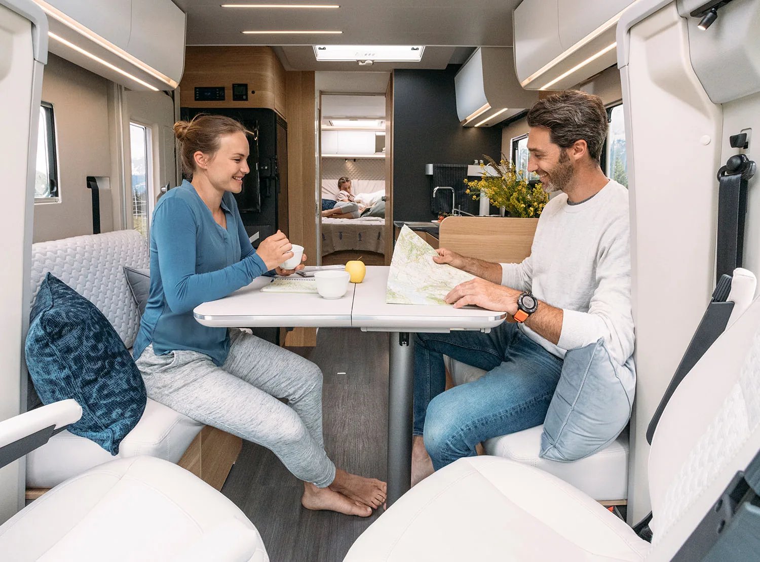 Adria Matrix 2026 - Reisende an der Dinette mit Blick auf die Berge durch das Panoramafenster