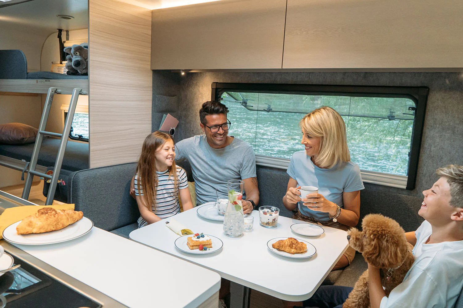 Familie sitzt gemeinsam an der Dinette im Wohnzimmer des Adria Altea mit Blick aus dem großen Seitenfenster