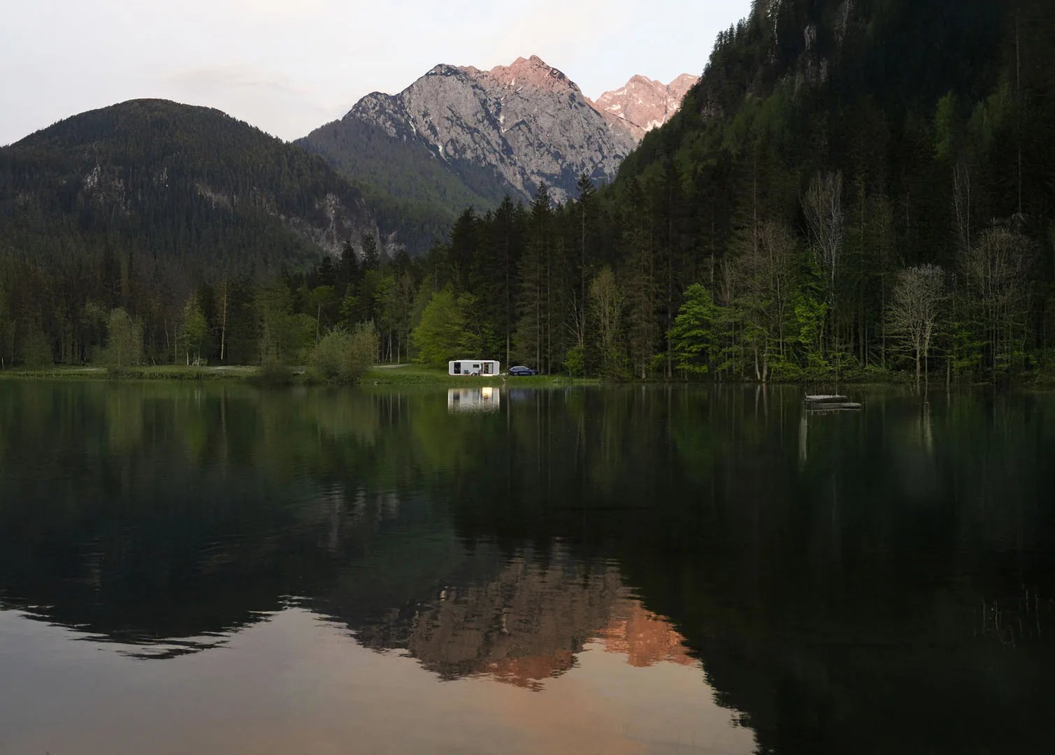 Adria Astella an einem Bergsee in der Abenddämmerung, Wohnwagen am Ufer zwischen Wald und Gipfeln