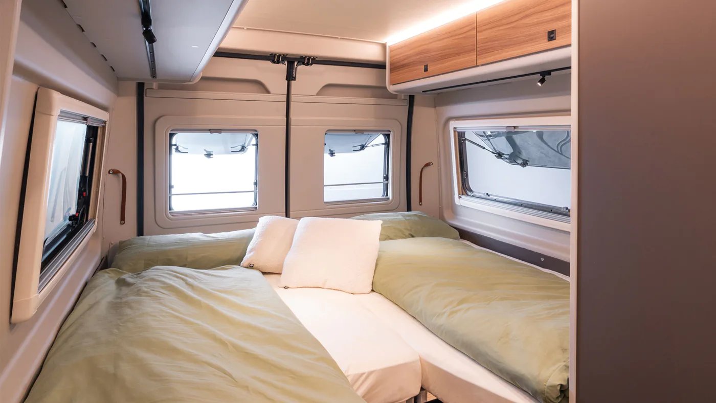 Zwei Längsbetten im Heck des Bürstner B66 Camper Van mit grüner Bettwäsche, Hecktürfenstern und Hängeschrank