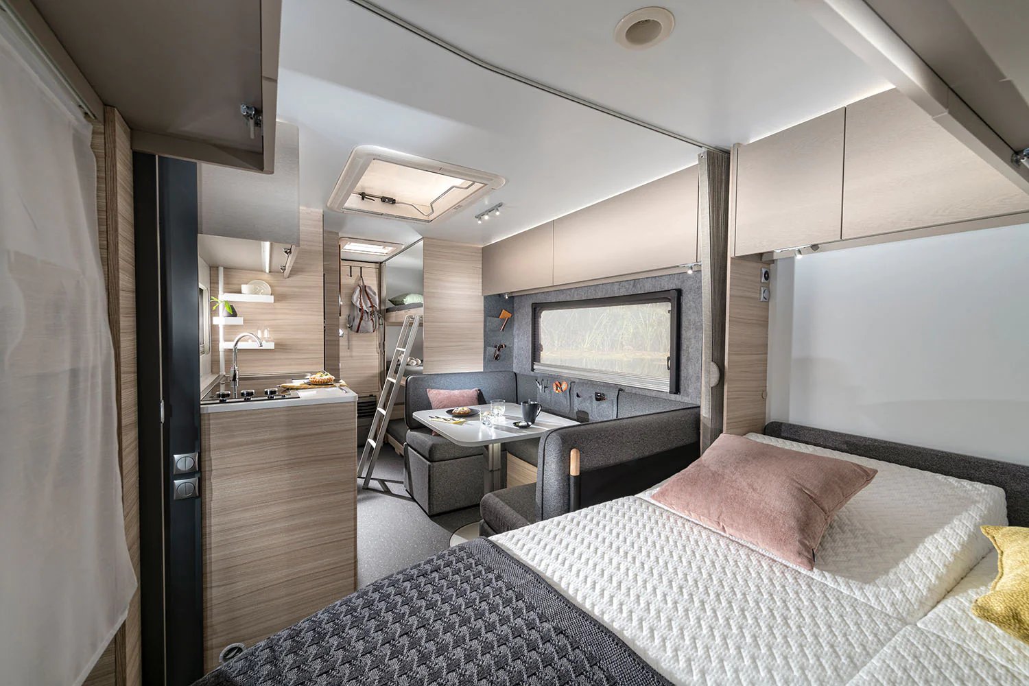 Offener Innenraum des Adria Altea mit Doppelbett im Vordergrund und Dinette samt Küche im Hintergrund