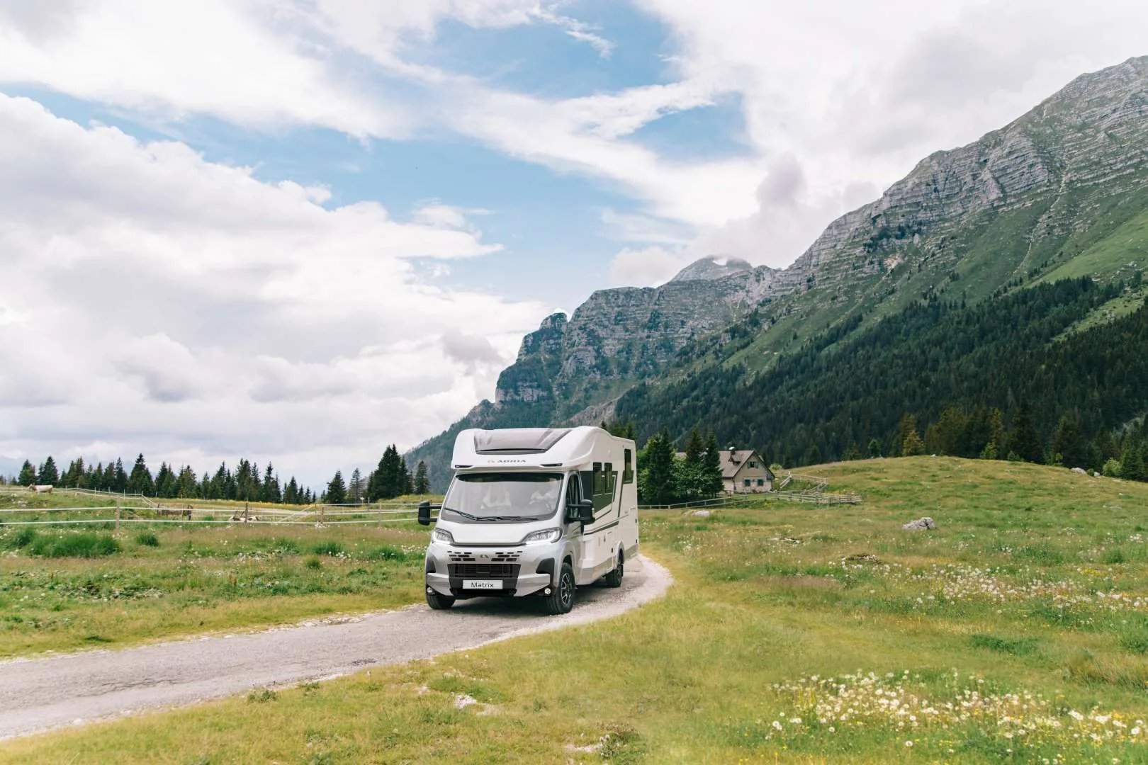 Adria Matrix 2026 auf Fiat-Basis, auf einer Alm-Zufahrt vor den Alpen, Panoramadachfenster im Dach sichtbar