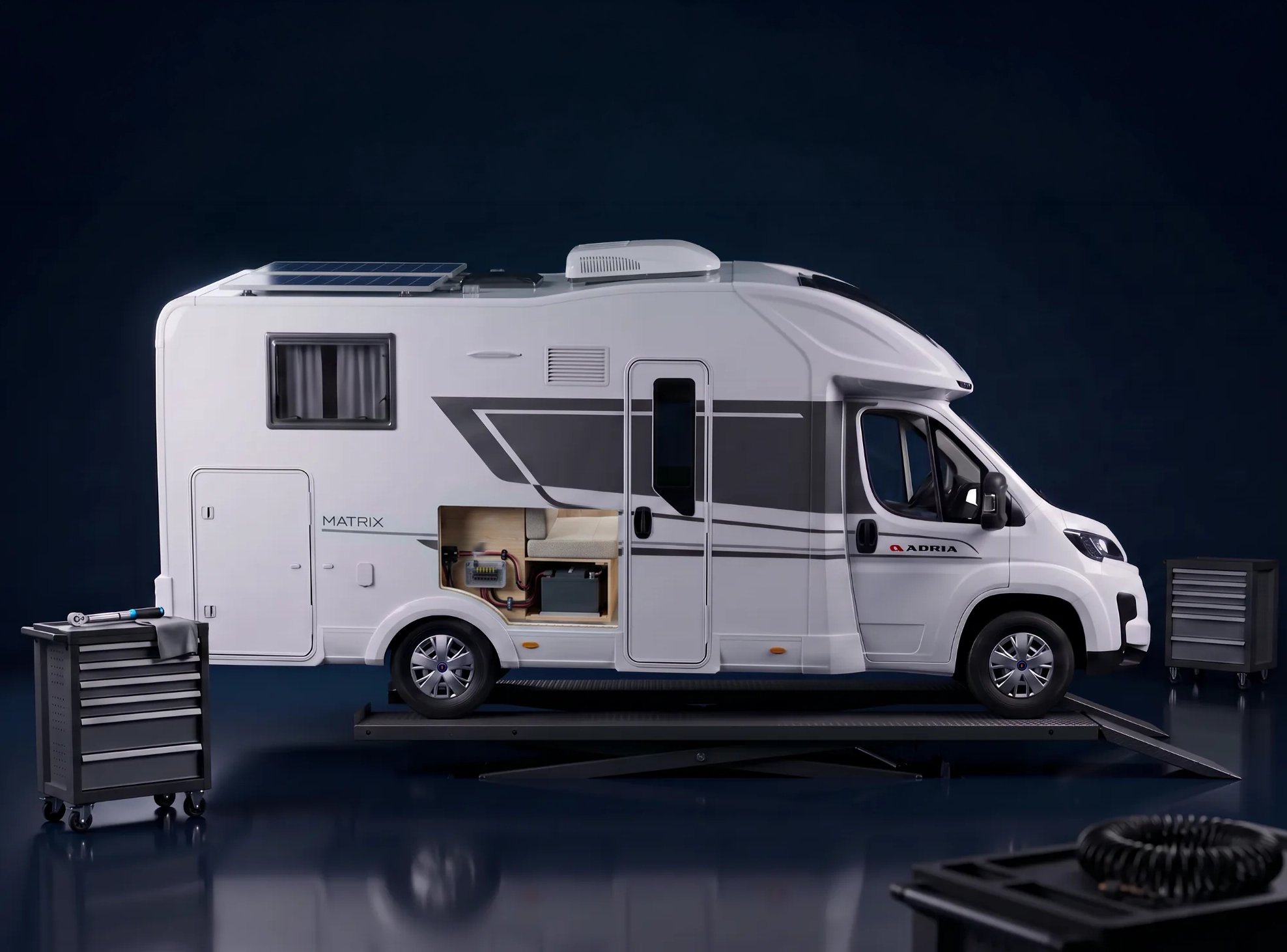 Teilintegriertes Reisemobil auf einer Doppelscheren-Hebebühne, links daneben ein Werkzeugwagen; auf dem Dach liegen ein Solarmodul und ein Dachklimagerät.